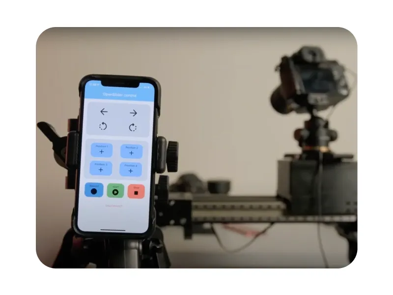 A phone running the OpenSlider control app, with arrow, rotate, position and record buttons, in front of a camera mounted on the slider.