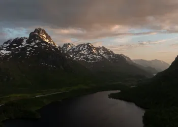Drone photo of snow-capped peaks and a dark lake in Norway, lit by a low sun.
